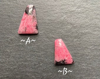May include: Two pink and black rhodochrosite cabochons, labeled A and B.