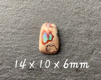 May include: A small, irregularly shaped opal cabochon with a white, brown, and red matrix. The opal has a blue and green iridescent flash. The stone measures 14 x 10 x 6 mm.