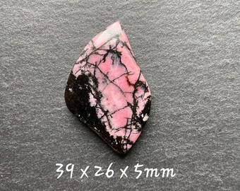 May include: A pink and black polished stone with a rough, irregular shape. The stone measures 3.9 x 2.6 x 0.5 inches.