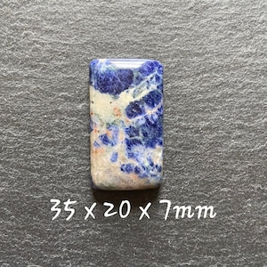Puede incluir: Un cabujón de piedra preciosa rectangular azul, blanco y naranja. La piedra mide 35 x 20 x 7 mm.