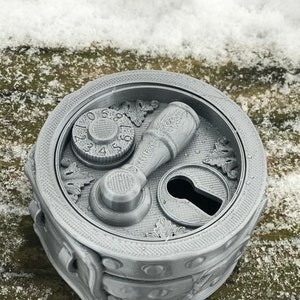 May include: A silver metal box with a combination lock, a keyhole, and a lever handle. The box has a decorative design with leaves and a textured surface.