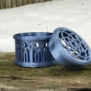 May include: A blue, 3D printed, decorative box with a geometric design on the lid and a gothic arch design on the sides. The box is open and the lid is lying next to it.