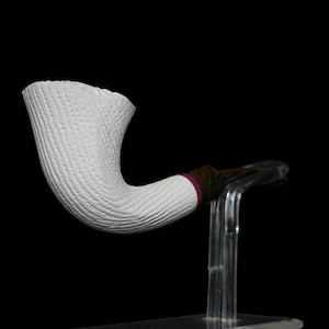 Peut inclure: Une pipe en céramique blanche avec une surface texturée, présentée sur un support en acrylique transparent. La pipe a une tige incurvée et une coupe avec une large ouverture.