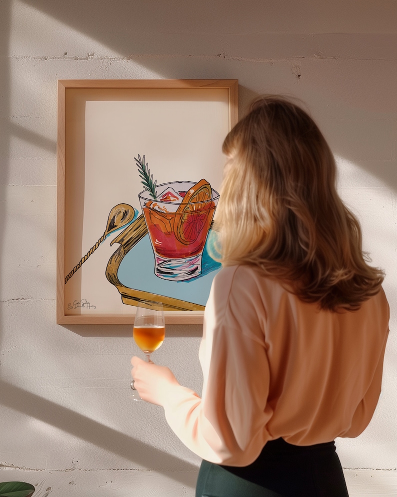 Puede incluir: Una ilustraci&oacute;n enmarcada de un c&oacute;ctel con una rodaja de naranja y una ramita de romero. La ilustraci&oacute;n es de estilo moderno con colores y l&iacute;neas atrevidas. La obra de arte est&aacute; colgada en una pared blanca.