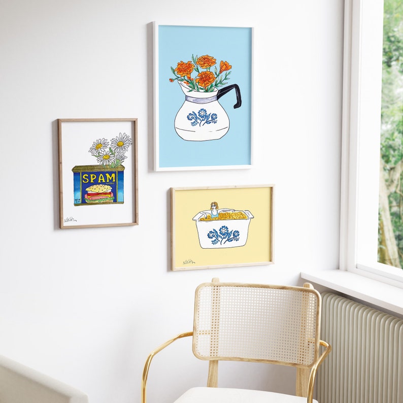 May include: Three framed prints with a blue and white floral theme. The top print features a blue and white pitcher with orange flowers. The middle print features a can of Spam with a daisy on top. The bottom print features a blue and white casserole dish with a yellow background.