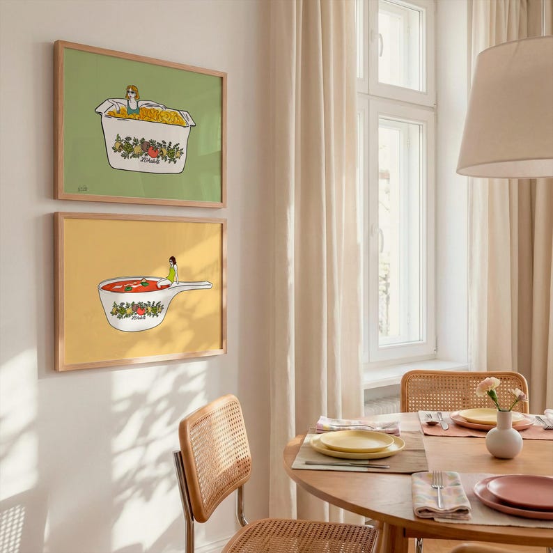 May include: Two framed art prints. The top print features a person in a box of pasta on a green background. The bottom print shows a person in a pot of tomato soup on a yellow background. Both prints have wooden frames.