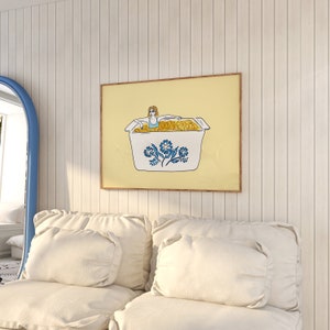 May include: A framed illustration of a woman in a blue swimsuit sitting in a white casserole dish filled with yellow macaroni. The dish has a blue and white floral design. The background is a light yellow color.