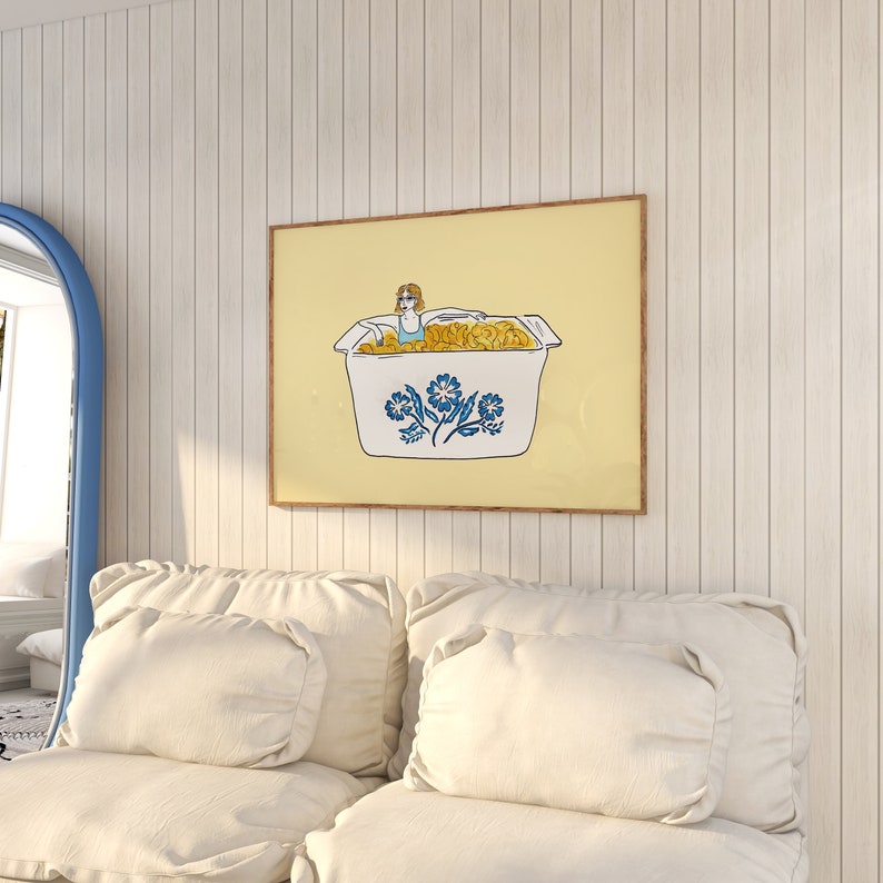 May include: A framed illustration of a woman in a blue swimsuit sitting in a white casserole dish filled with yellow macaroni. The dish has a blue and white floral design. The background is a light yellow color.