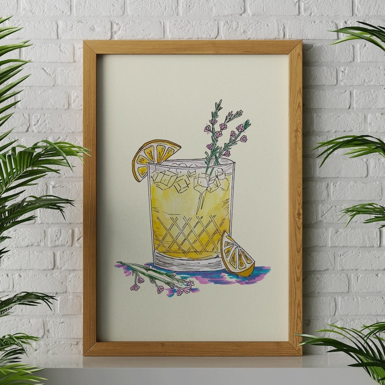 May include: A framed illustration of a yellow cocktail with a lemon wedge and a sprig of flowers. The drink is in a glass with a checkered pattern. The illustration is on a cream background.