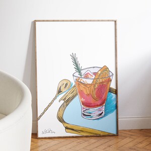 Puede incluir: Una ilustraci&oacute;n enmarcada de un c&oacute;ctel con una rodaja de naranja y una ramita de romero en una bandeja azul. El c&oacute;ctel est&aacute; en un vaso con hielo y una pajita. La ilustraci&oacute;n est&aacute; firmada "Big Cat Studio".