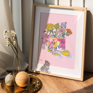 framed illustration of two cans of La Croix sparkling water with pink, yellow, and green flowers. The cans are on a pink background with a shadow of the flowers behind them. The text on the cans reads 'La Croix'.