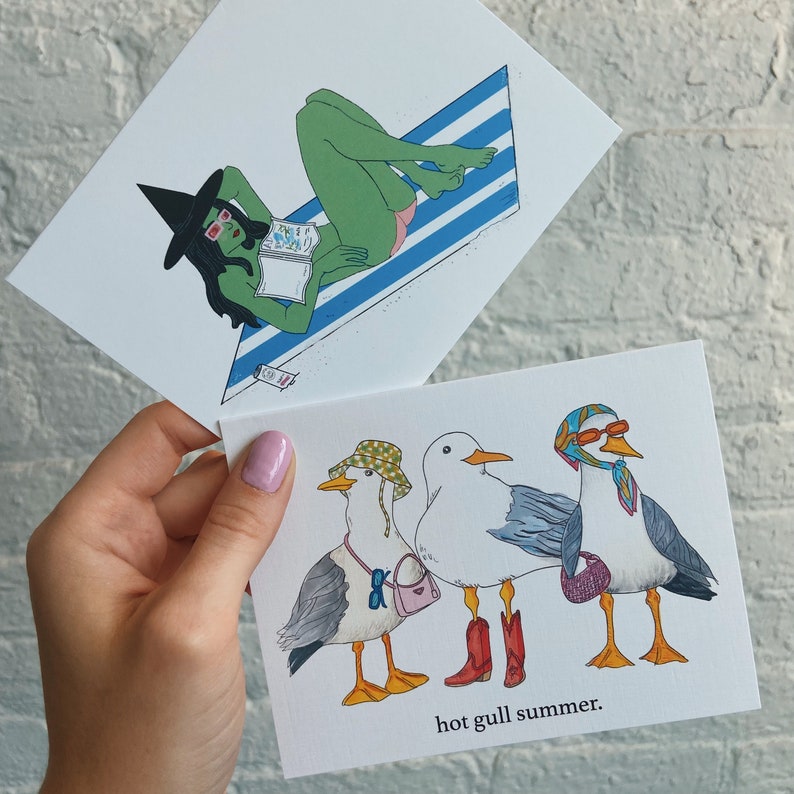 May include: A card featuring a cartoon illustration of three seagulls wearing sunglasses and hats. The seagulls are standing on a white background with the text "hot gull summer."