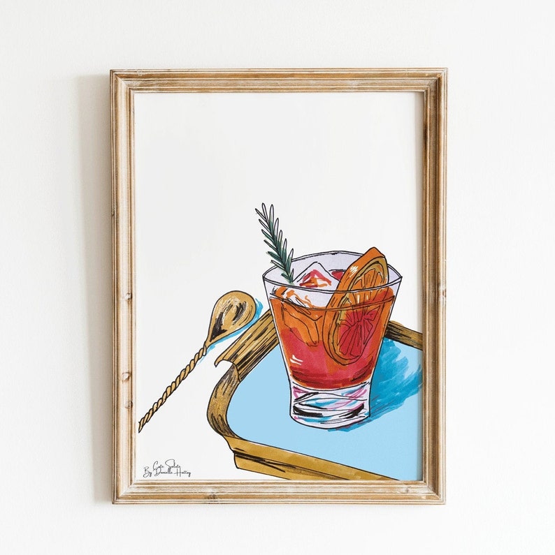 Puede incluir: Una ilustraci&oacute;n dibujada a mano de un c&oacute;ctel en un vaso con hielo, una rodaja de naranja y una ramita de romero. El c&oacute;ctel est&aacute; en una bandeja dorada con un fondo azul. La ilustraci&oacute;n est&aacute; enmarcada en un marco de madera claro.