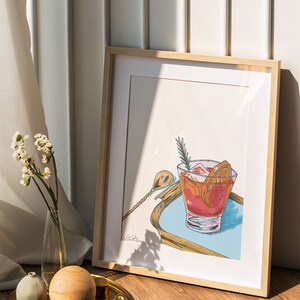 Puede incluir: Una ilustraci&oacute;n enmarcada de un c&oacute;ctel en un vaso con hielo, rodajas de naranja y una ramita de romero. El vaso est&aacute; sobre una bandeja azul y dorada con un agitador plateado.