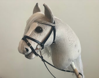 Caballo de juguete gris con puntos oscuros y crin blanca, con brida y riendas.