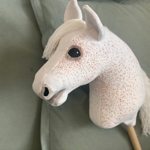 Puede incluir: Caballo de balanc&iacute;n de peluche blanco con manchas marrones y una crin y cola blancas. El caballo tiene ojos negros y un palo de madera para el cuerpo.