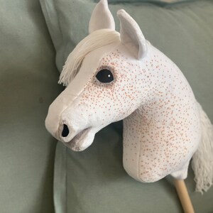 Puede incluir: Un caballo de balanc&iacute;n de peluche blanco con manchas marrones y ojos negros. El caballo tiene una larga melena y cola blancas.