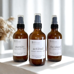 Könnte beinhalten: Drei braune Glassprühflaschen mit schwarzen Sprühköpfen und weißen Etiketten. Die Etiketten lauten "eternity", "actitud" und "the island". Die Flaschen sind mit "Room and Linen Spray" beschriftet und haben 118 ml.