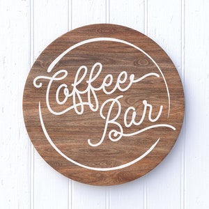 Könnte beinhalten: Ein rundes Holzschild mit einem weißen Kreis und dem Text "Coffee Bar" in einer kursivschrift.