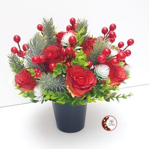 May include: A floral arrangement in a black pot featuring red roses, bright red berries, green foliage, and white-tipped pine sprigs. A small circular logo on the lower right contains the text A Little Bit of Nice Christmas Shop Details.
