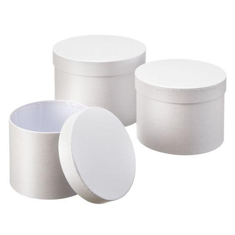 May include: Three cylindrical white gift boxes with matching lids. Two of the boxes are closed, while one box is open with its circular lid placed upright in front of it. The containers feature a smooth, matte finish and a simple, clean design.