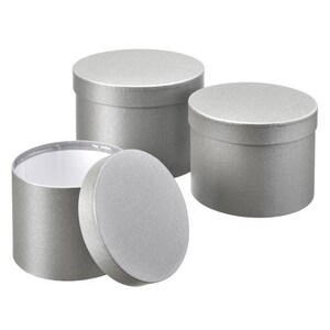 May include: Three cylindrical gift boxes with a metallic silver finish. Two boxes are closed with matching lids, while one box is open with its circular lid placed upright in front of it, revealing a plain white interior lining.