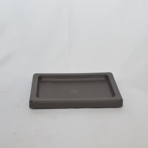 May include: A square, dark brown, ceramic plant saucer with a slightly raised edge.