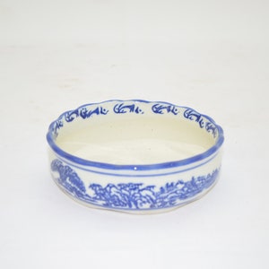 May include: A small, white ceramic bowl with a blue and white floral design. The bowl has a scalloped rim and a slightly rounded bottom.
