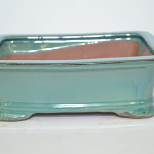 May include: A rectangular, light green ceramic bonsai pot with a brown interior and four small feet.