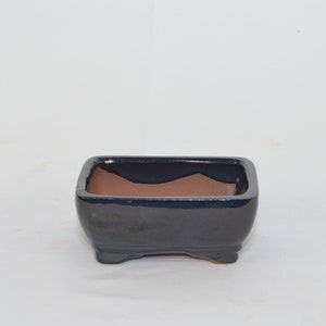 May include: A rectangular ceramic bonsai pot with a dark blue glaze and a brown clay interior. The pot has four small feet.