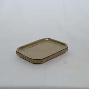 May include: A rectangular, light brown ceramic tray with a slightly raised edge. The tray has a speckled finish and a slightly irregular shape.