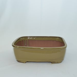 May include: A rectangular ceramic bonsai pot with a light brown glaze. The pot has a slightly rounded bottom and four small feet.