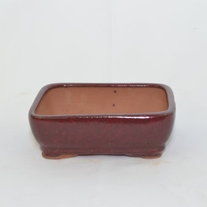 May include: A square, red-brown bonsai pot with a slightly rounded bottom and four small feet.