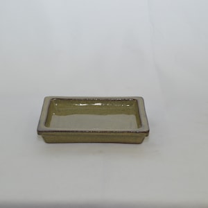 May include: A square, light green ceramic saucer with a slightly raised rim. The saucer has a glazed finish and a subtle speckled texture.