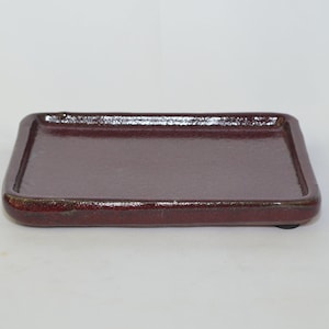 May include: A rectangular, burgundy-colored ceramic tray with rounded corners. The tray has a glossy finish and a slightly raised edge. The tray is approximately 6 inches long and 4 inches wide.
