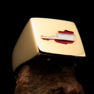 May include: A gold ring with a square top featuring a red and white enamel outline of Austria. The ring is on a brown surface.