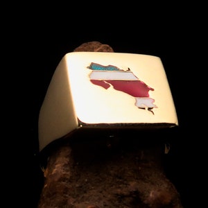 Op de afbeelding: Een goudkleurige ring met een rechthoekige voorkant. De voorkant heeft een ingelegde kaart van Costa Rica in rood, wit en turquoise. De ring staat tegen een donkere achtergrond.