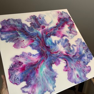Puede incluir: Pintura abstracta con colores p&uacute;rpura, rosa y azul que se arremolinan sobre un fondo blanco. Los colores crean una forma de flor en el centro del lienzo.