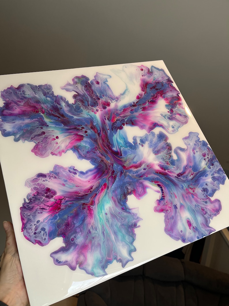 Puede incluir: Pintura abstracta con colores p&uacute;rpura, rosa y azul que se arremolinan sobre un fondo blanco. Los colores crean una forma de flor en el centro del lienzo.