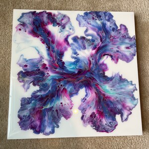 Puede incluir: Pintura abstracta sobre lienzo con colores azules, morados y rosas en espiral. La pintura tiene un fondo blanco y un punto amarillo claro en el centro.