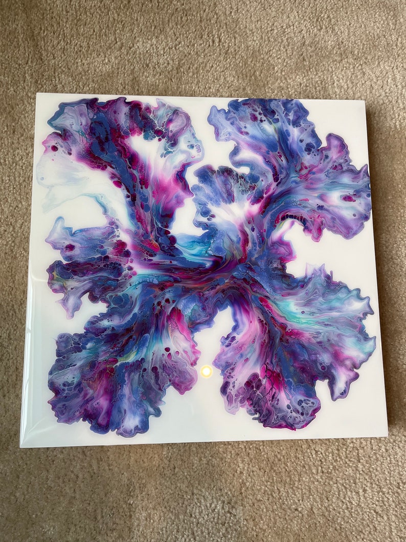 Puede incluir: Pintura abstracta sobre lienzo con colores azules, morados y rosas en espiral. La pintura tiene un fondo blanco y un punto amarillo claro en el centro.