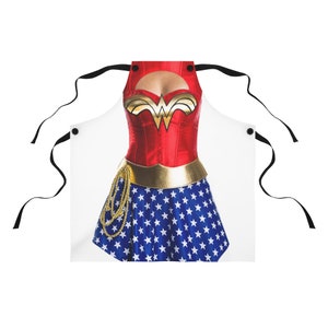 Pu&ograve; includere: Un grembiule bianco con un design di Wonder Woman. Il grembiule presenta un corpetto rosso con una cintura dorata e una gonna blu con stelle bianche. Il grembiule ha due bretelle nere.