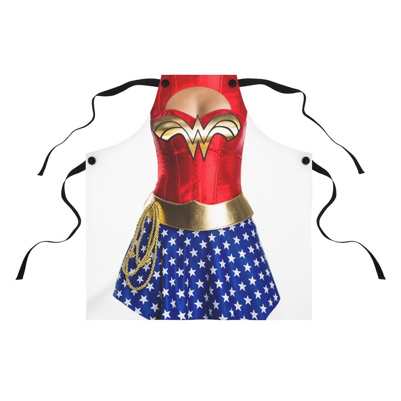 Pu&ograve; includere: Un grembiule bianco con un design di Wonder Woman. Il grembiule presenta un corpetto rosso con una cintura dorata e una gonna blu con stelle bianche. Il grembiule ha due bretelle nere.