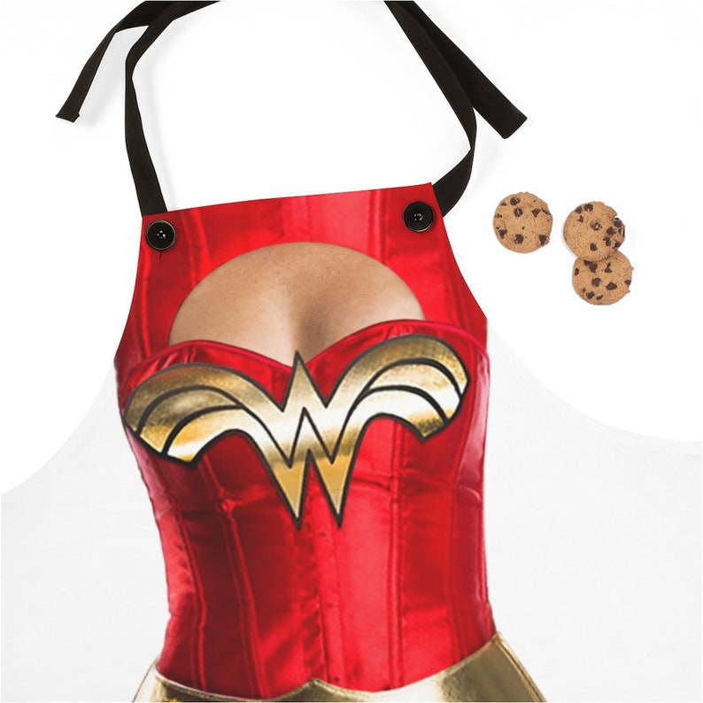 Pu&ograve; includere: Grembiule rosso e oro di Wonder Woman con un'apertura per il petto. Il grembiule ha bretelle nere e due bottoni neri.