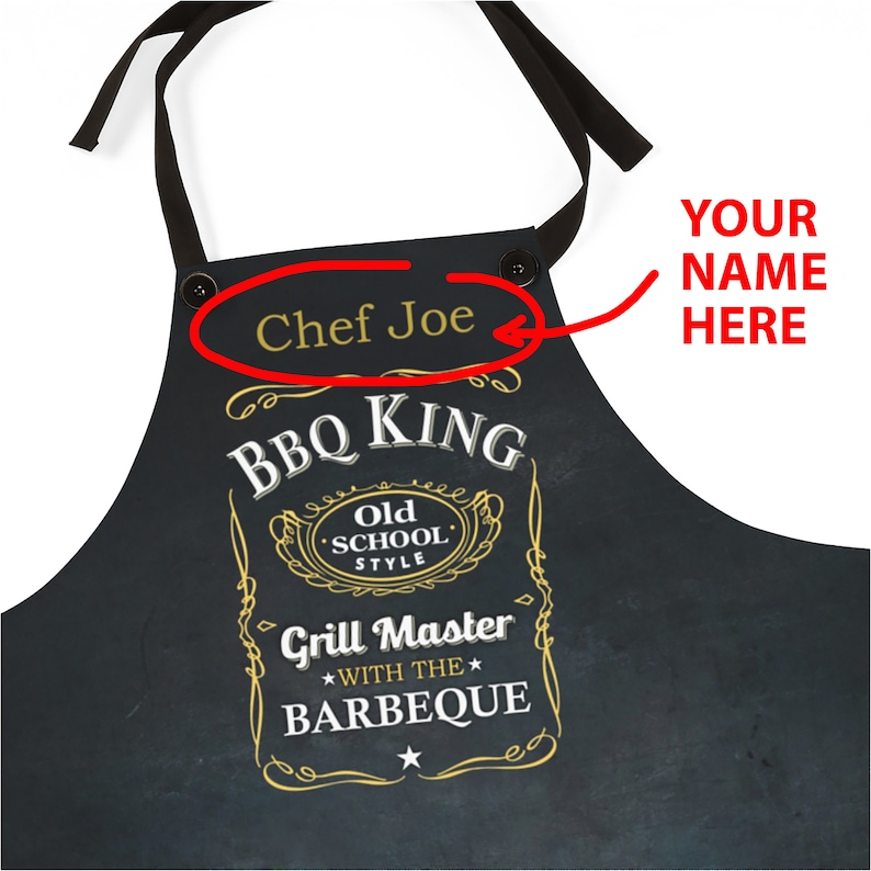 Puede incluir: Delantal negro con un dise&ntilde;o dorado y blanco que dice "BBQ King" y "Grill Master with the Barbeque". El delantal tiene una etiqueta de nombre personalizable que dice "Chef Joe".
