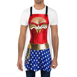 Pu&ograve; includere: Un grembiule bianco con un design di Wonder Woman. Il grembiule presenta un corpetto rosso con una stella dorata e una gonna blu con stelle bianche.