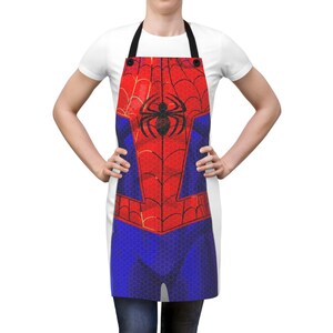 Pu&ograve; includere: Un grembiule rosso, blu e nero con un design a costume di Spider-Man. Il grembiule ha un cinturino nero per il collo e un grande emblema di ragno nero sul petto. Il grembiule &egrave; indossato da una persona.