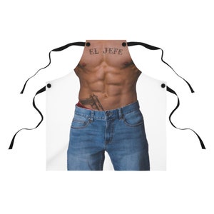 Pu&ograve; includere: Grembiule bianco con una grafica di un busto muscoloso con il tatuaggio "EL JEFE" e una pistola infilata in jeans blu. Lacci neri e dettagli con bottoni completano il design.