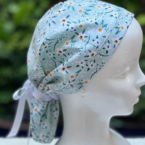 K&ouml;nnte beinhalten: Eine hellblaue OP-M&uuml;tze mit wei&szlig;em Blumenmuster. Die M&uuml;tze hat einen Bindfaden am R&uuml;cken.