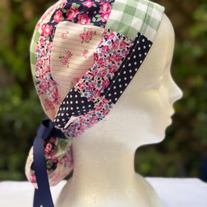 May include: A patchwork scrub cap featuring a variety of floral and polka dot patterns in pink, blue, and white. The cap includes a navy blue ribbon for tying. The cap is displayed on a white mannequin head.